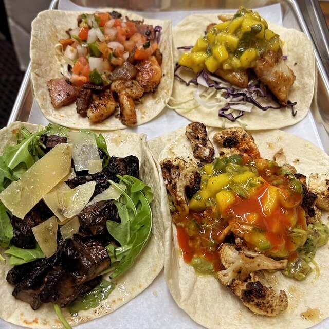 4 tacos on a plate with salsa toppings