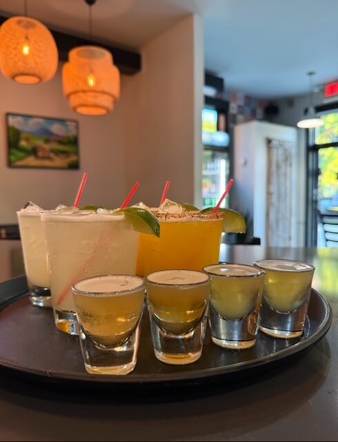 shots and cocktails garnished with limes on a tray